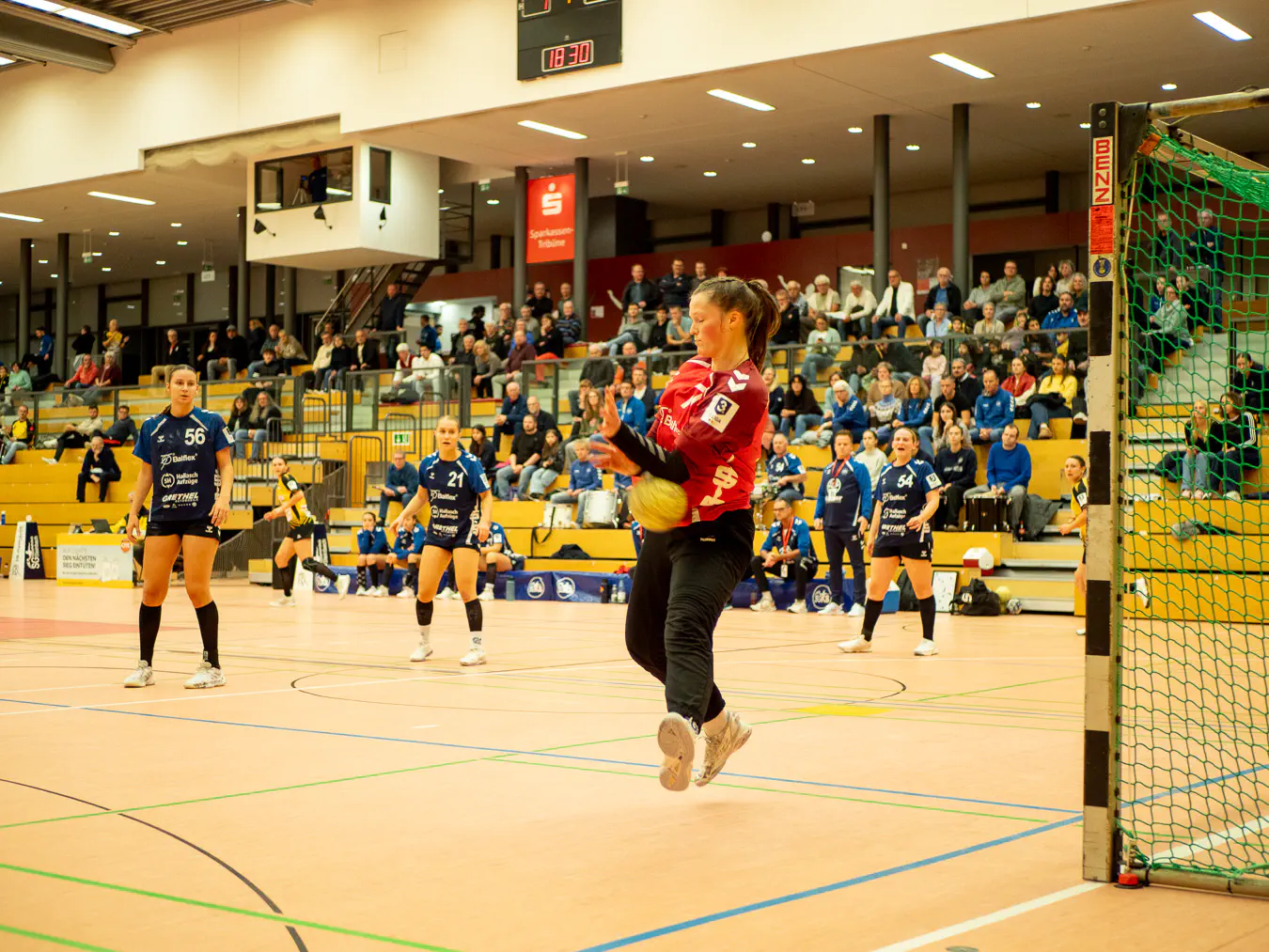 Eine Torfrau im Sprung kurz davor, einen Ball zwischen Unterarm und Oberschenkel einzuklemmen.