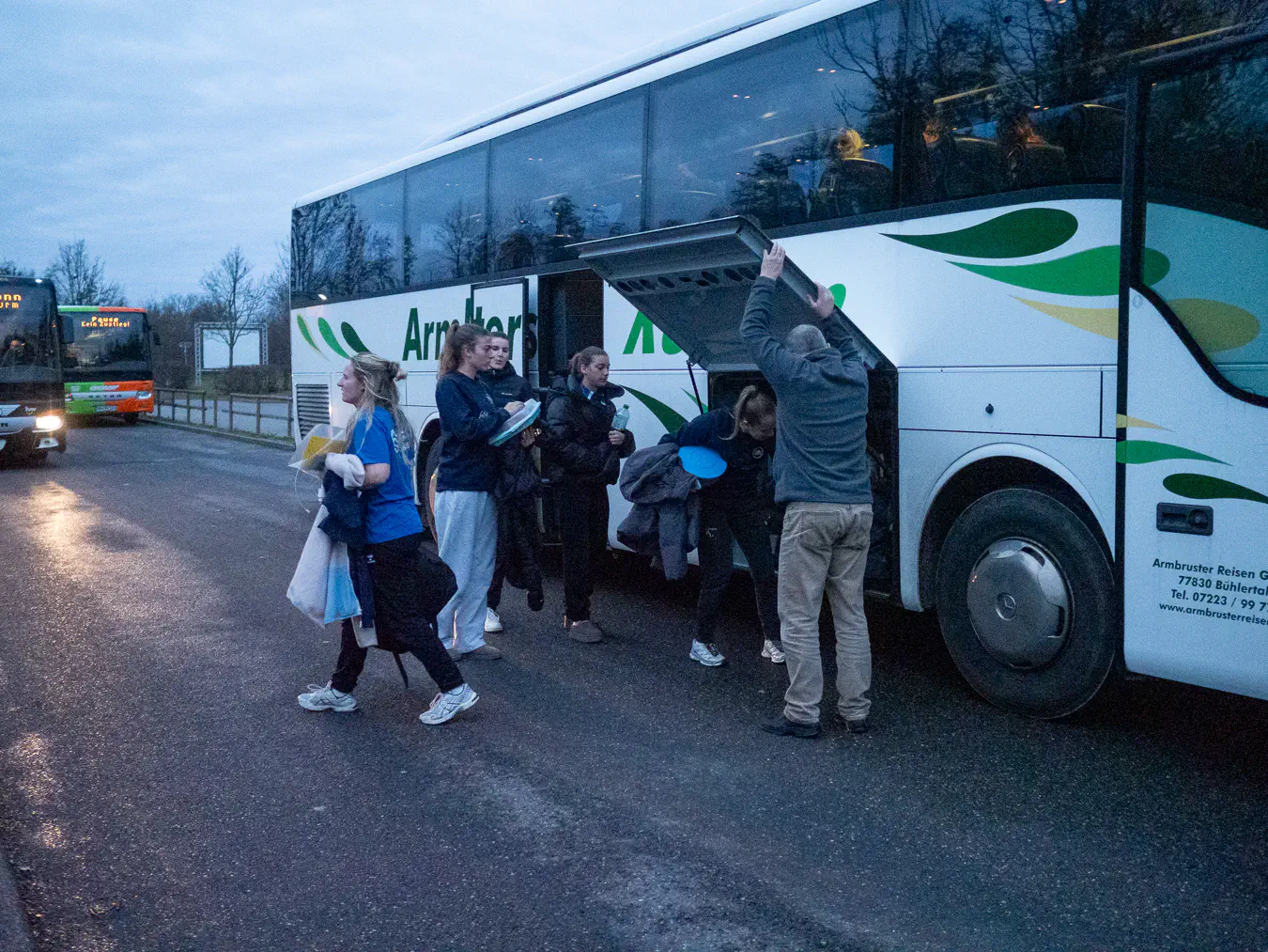 Spielerinnen der SG Kappelwindeck/Steinbach laden im Dämmerlicht ihr Gepäck aus einem Reisebus.