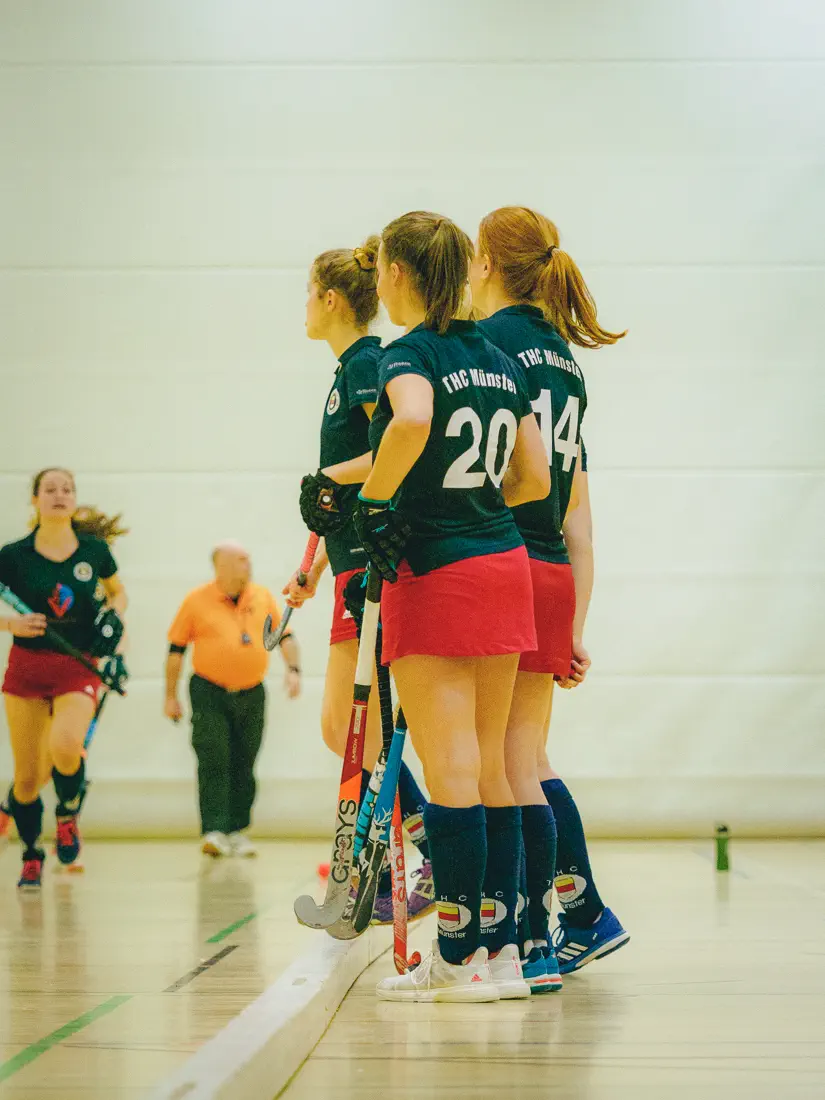 Drei Frauen in schwarzen Trikots stehen am Spielfeldrand