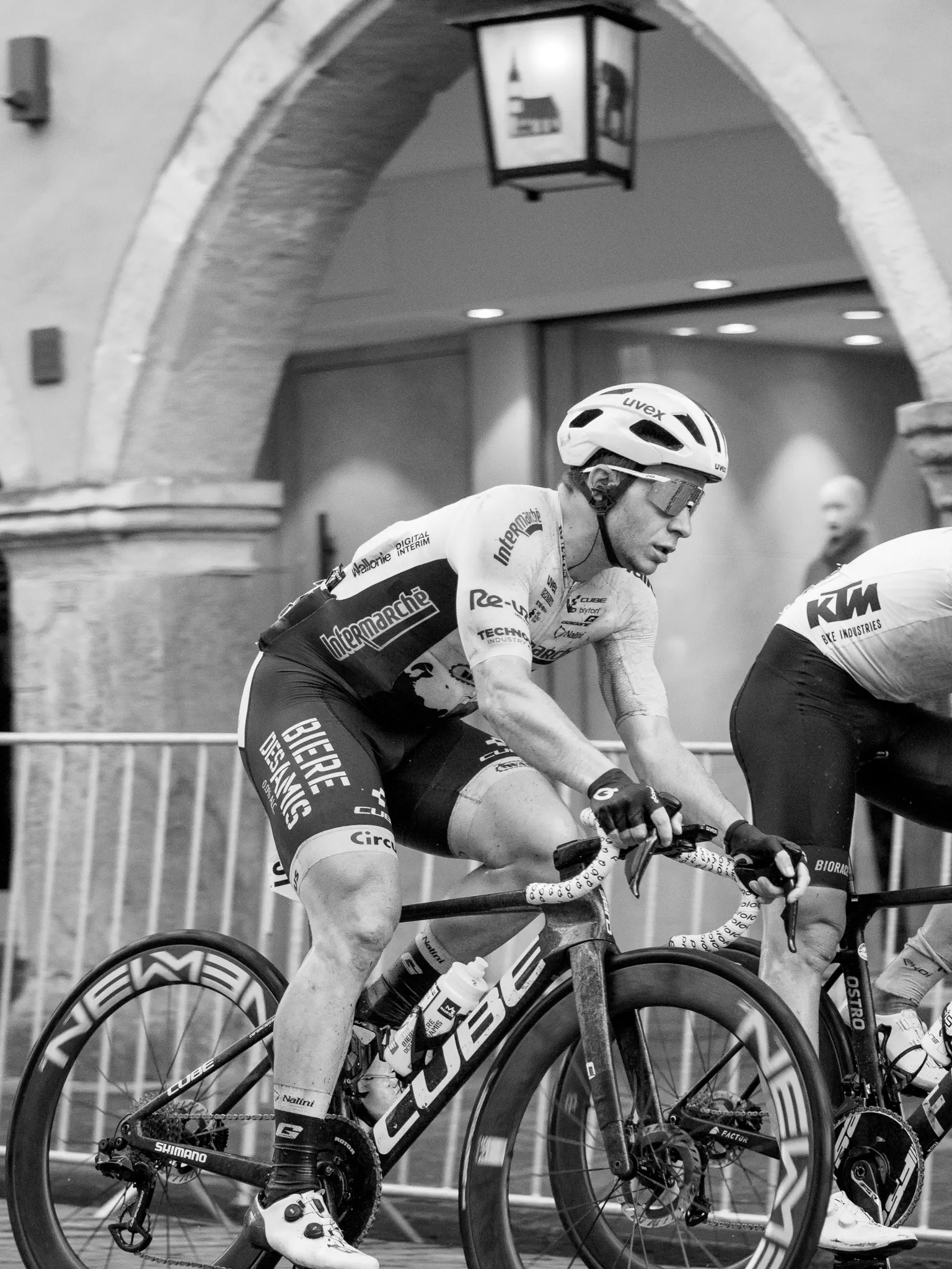 Ein Radfahrer fährt von links nach rechts durchs Bild, dahinter Absperrgitter, dahinter Arkaden