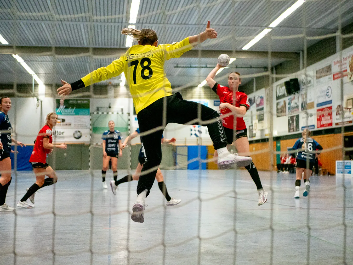 Die Kappelwindecker Torfrau streckt im Sprung alle Viere von sich, während im Hintergrund eine Schozacher Angreiferin zum Wurf ausholt