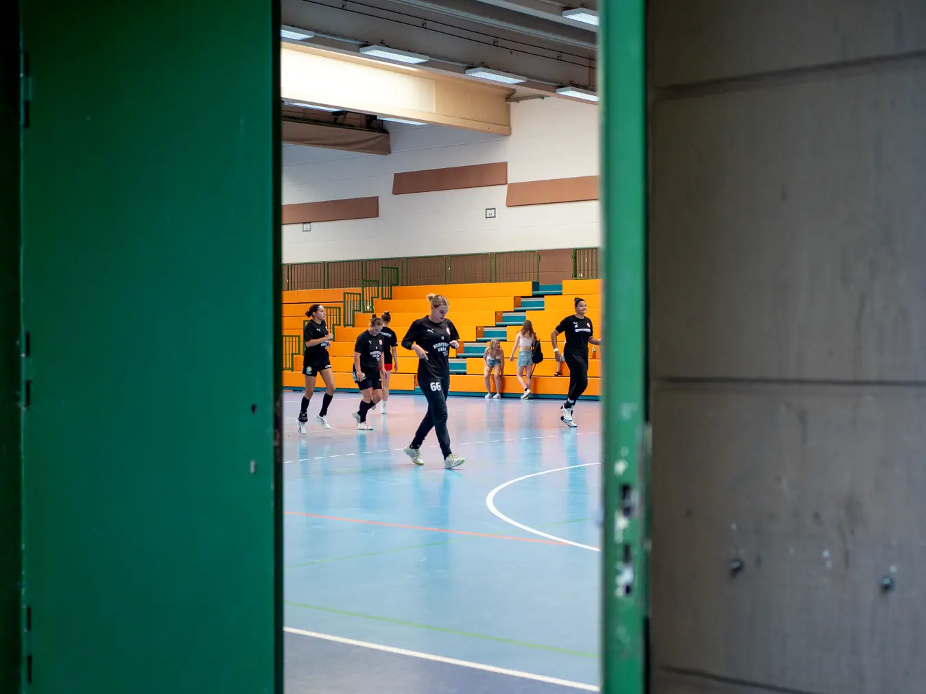 Frauen laufen in einer Sporthalle, Blick von außen durch eine offene Tür