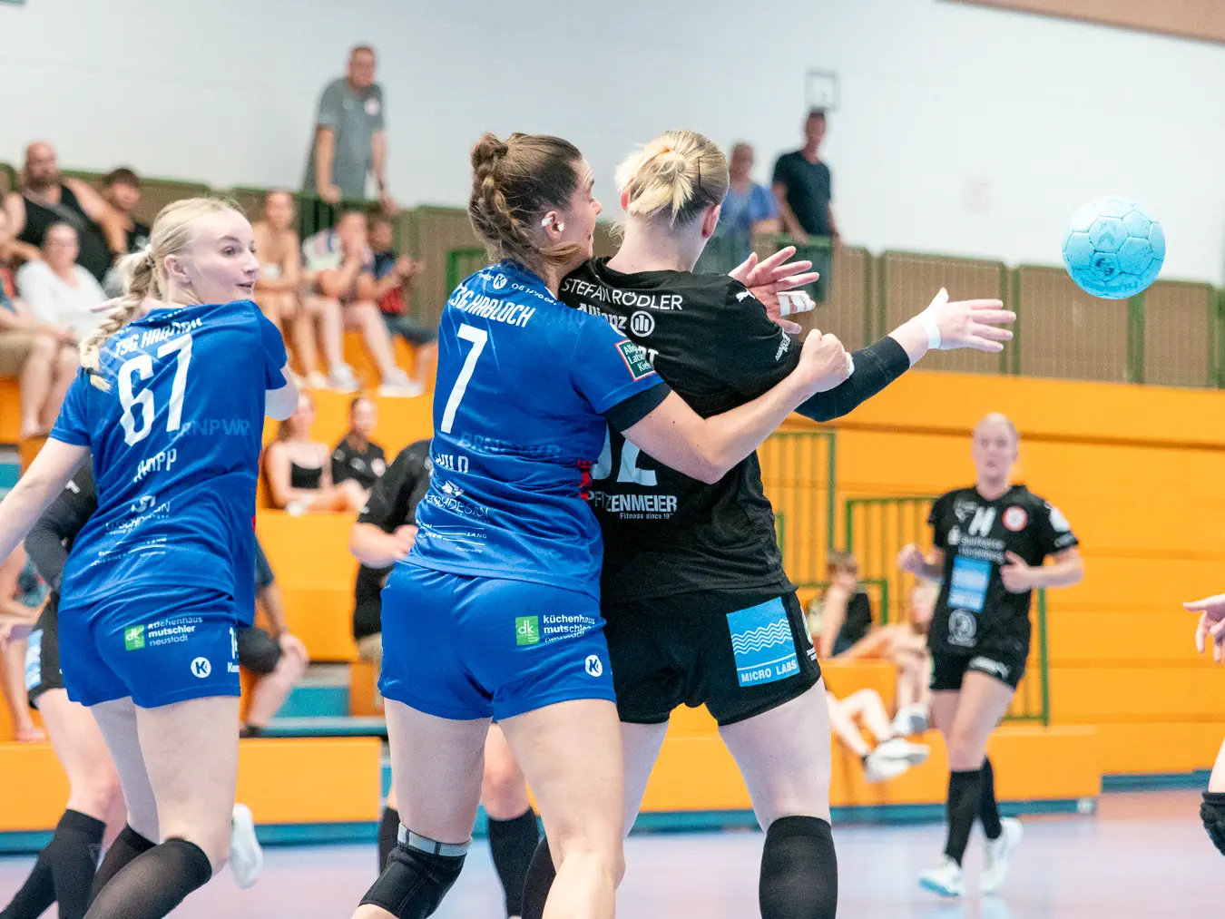 Zwei Frauen von hinten, die eine umklammert die andere, seitlich fliegt ein Ball weg