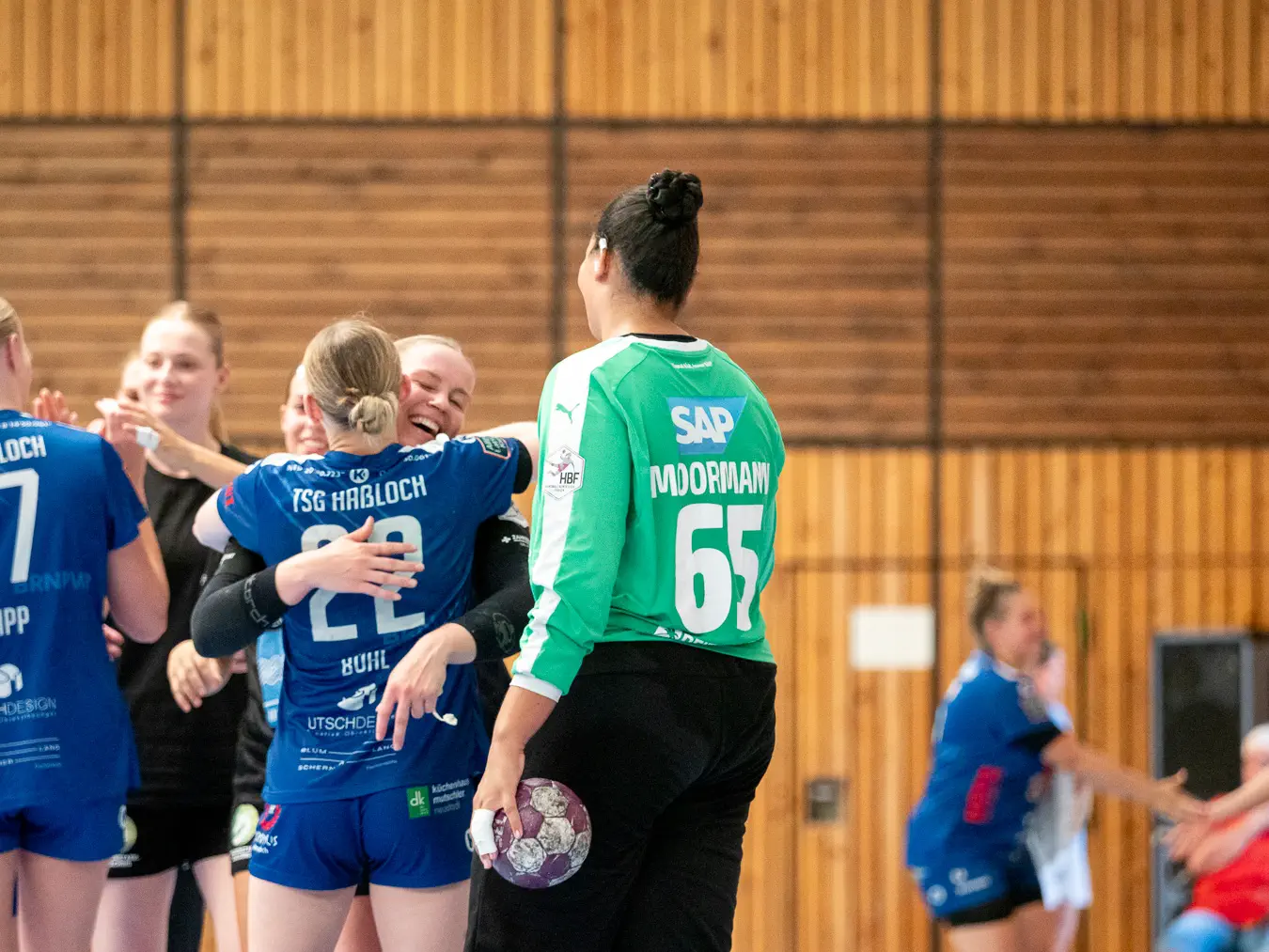 Zwei Frauen umarmen sich, eine dritte schaut zu