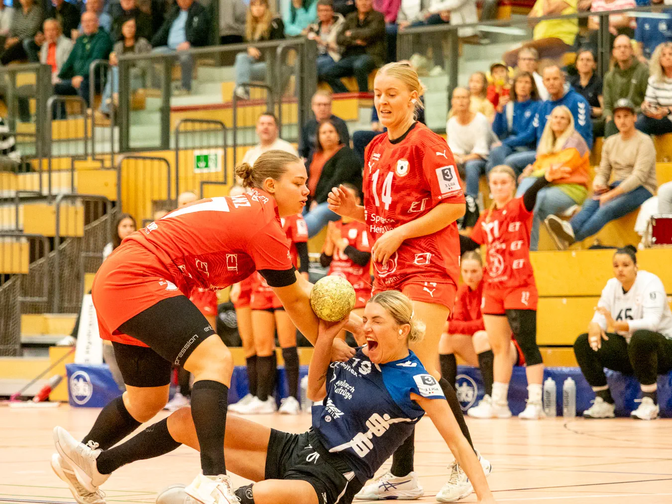 Eine Frau fällt schreiend zu Boden, eine weitere Frau darüber gebeugt hält die erste fest. Eine dritte Frau im Hintergrund schaut zu.