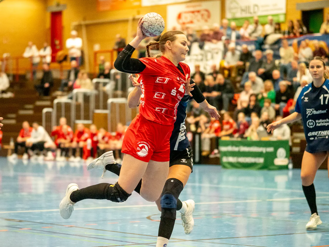 Eine Spielerin im roten Trikot im Sprungwurf wird seitlich von einer Spielerin im blauen Trikot gehalten.