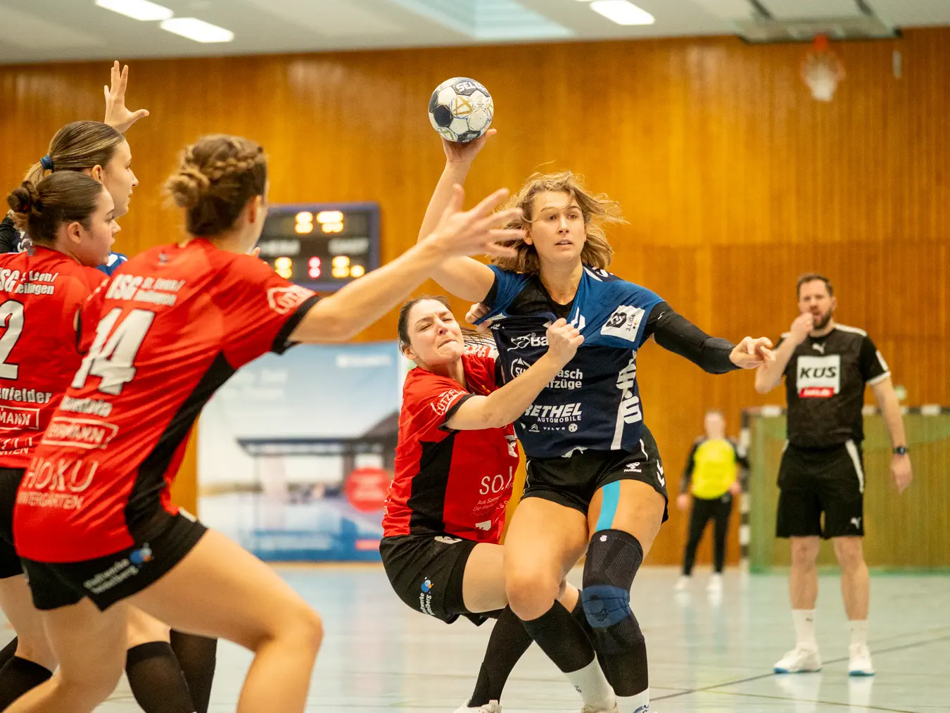 Eine Spielerin im blauen Trikot holt zum Wurf aus, eine Spielerin im roten Trikot hängt an ihrem Trikot.