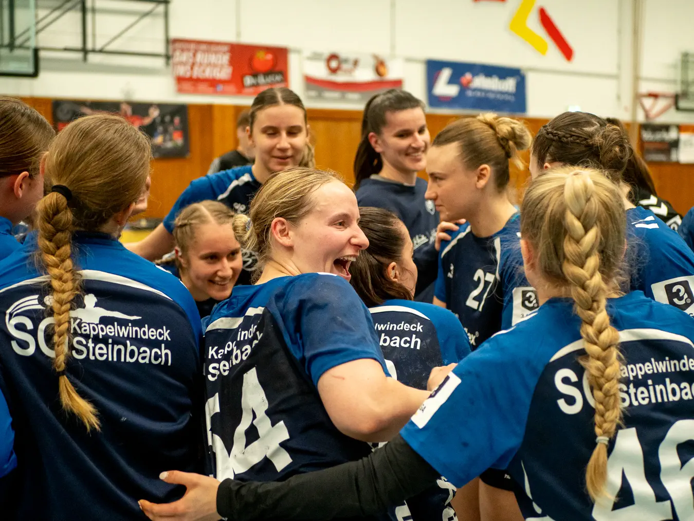 Spielerinnen in blauen Trikots stehen sich umarmend im Kreis, einige jubeln.