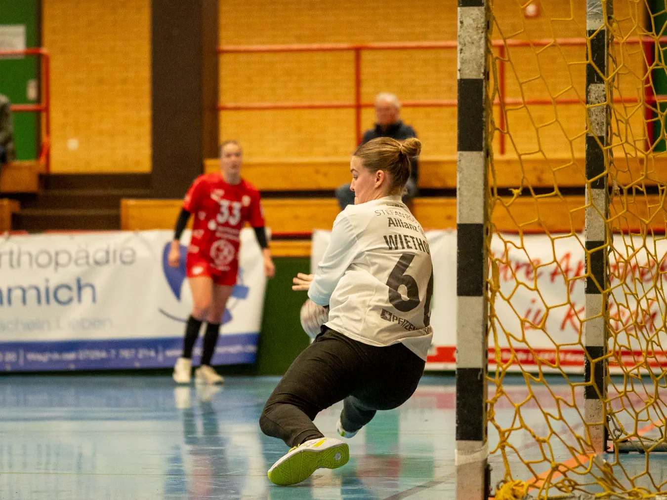 Eine Torfrau im weißen Trikot im Fall hält einen Ball.