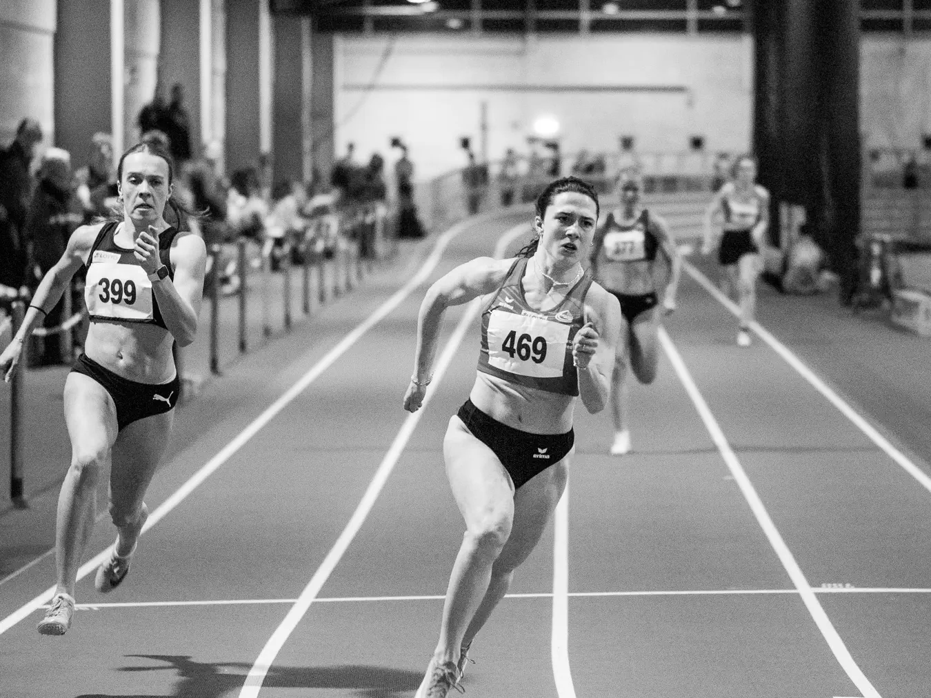 Eine Athletin rennt eine Rundbahn entlang auf die Kamera zu. Im Hintergrund unscharf weitere Athletinnen.