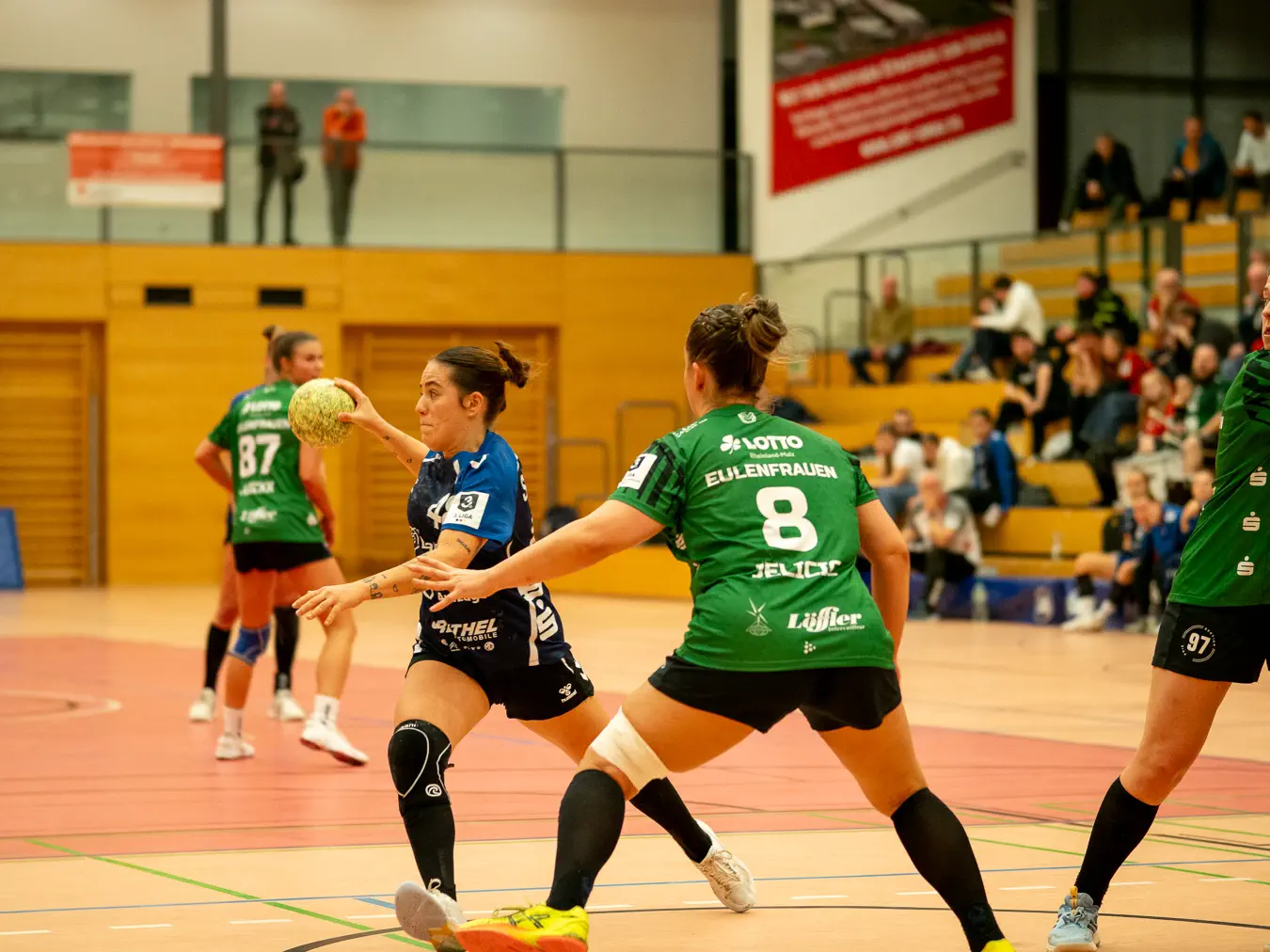 Eine Angreiferin mit Ball in der Hand läuft quer zum Kreis, davor zwei nachschiebende Verteidigerinnen.