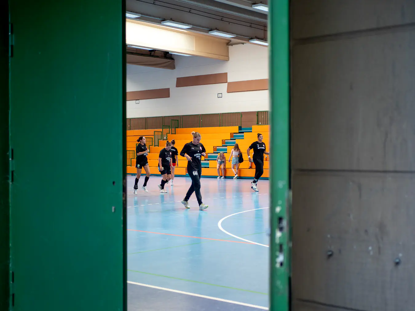 Frauen laufen in einer Sporthalle, Blick von außen durch eine offene Tür